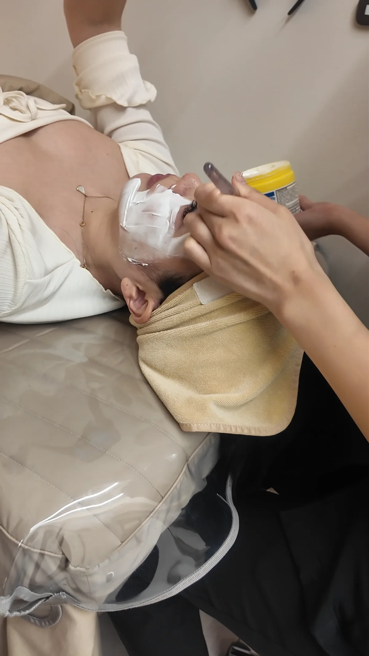 Person on a treatment bed while a clinician's gloved hands prepare the face