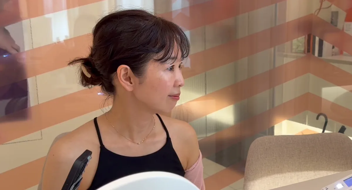 A woman in a black sleeveless top with a pink wrap over one shoulder sits in a clinic room.