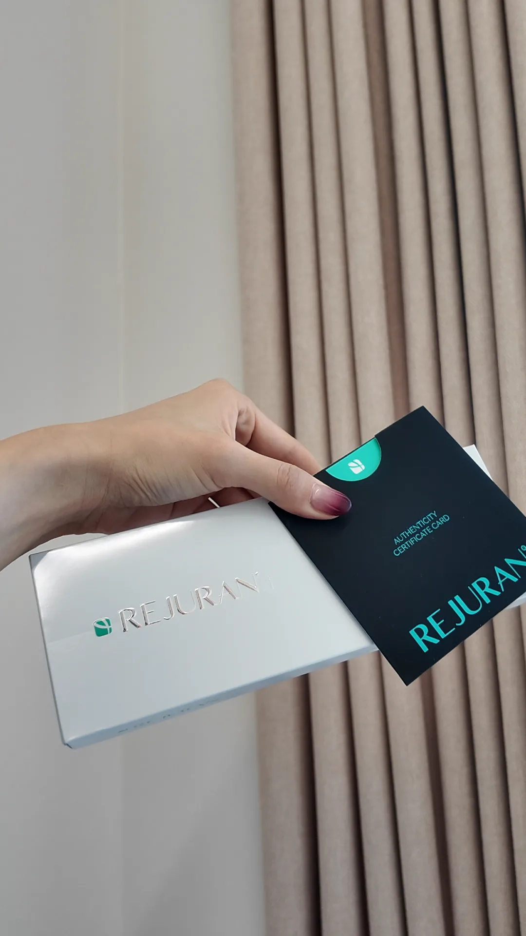 Hands holding two Rejuran product boxes against a curtain