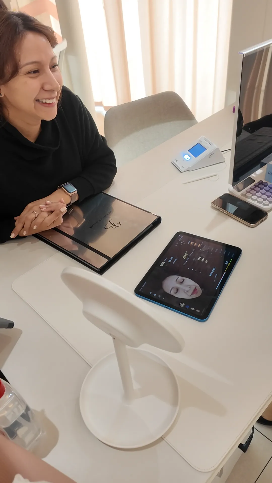 Woman seated at a clinic table looking toward a tablet