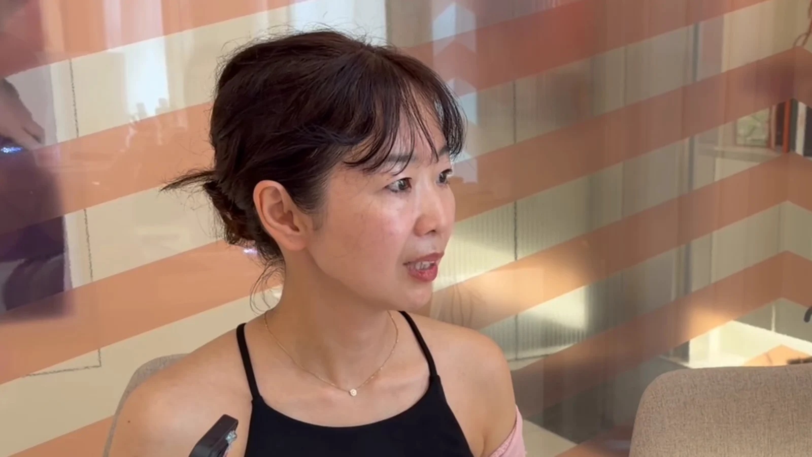 A woman in a black sleeveless top with a pink wrap sits in a clinic room.