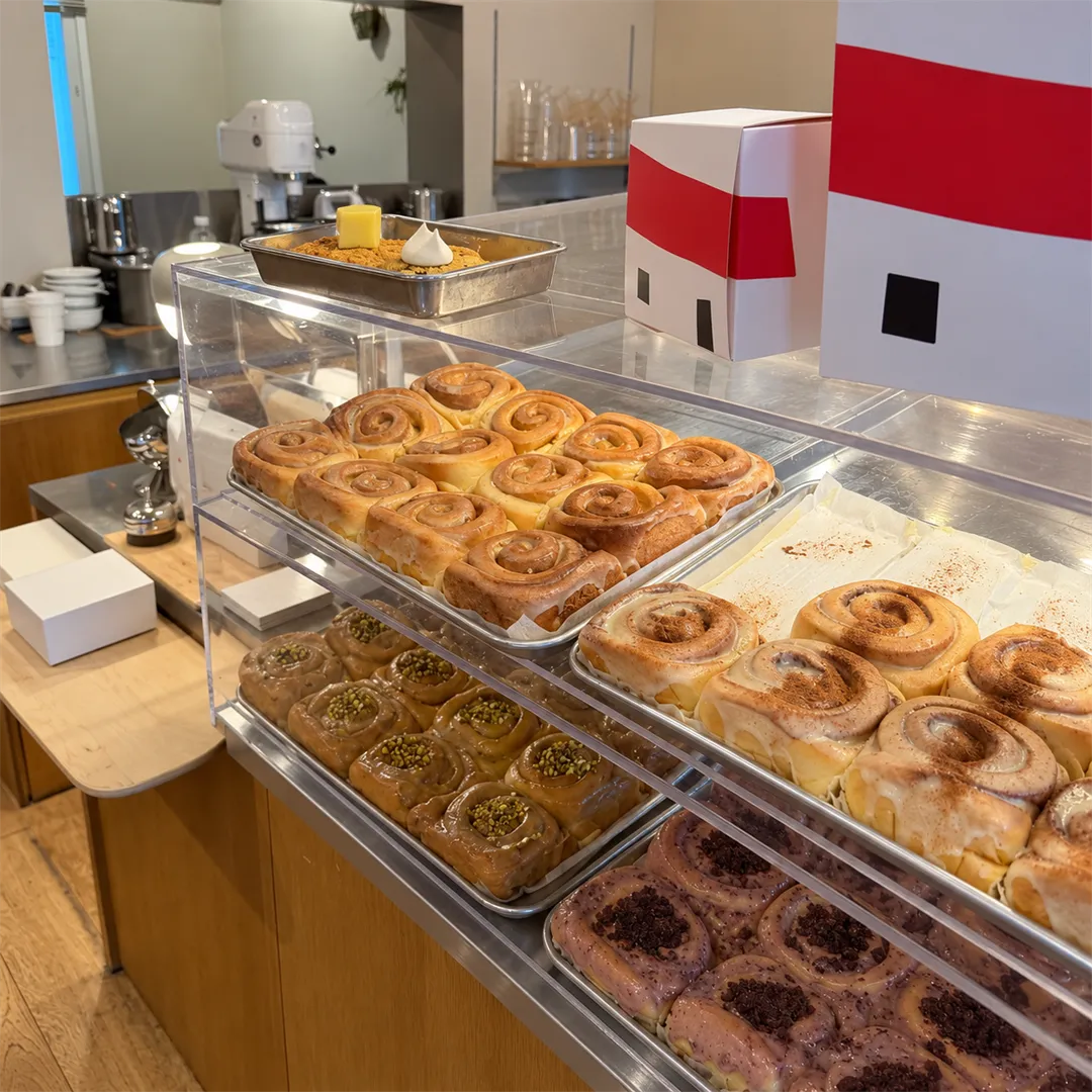 Two-tier glass display case with brown rolls, iced rolls and green-topped pastries
