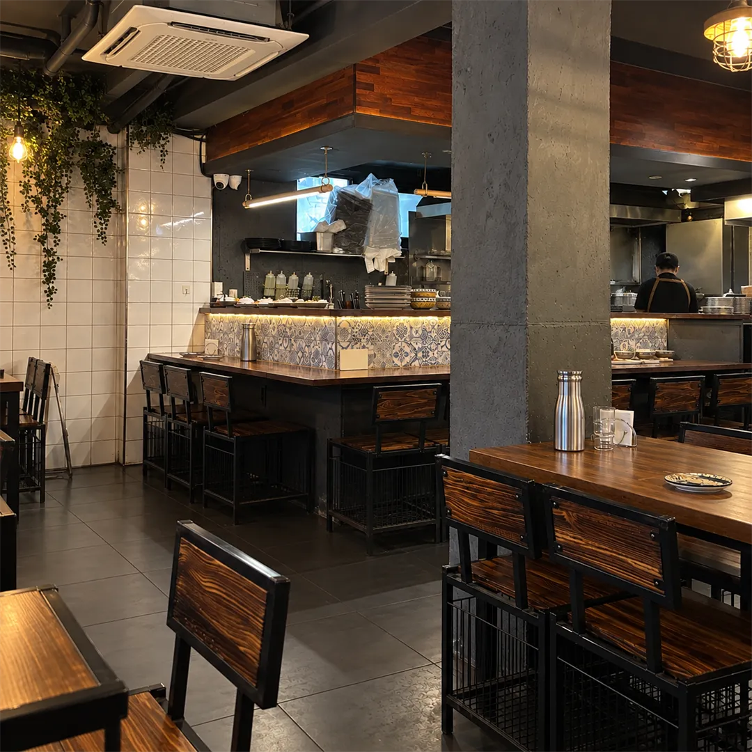 Open kitchen and wooden tables with a concrete pillar inside the restaurant
