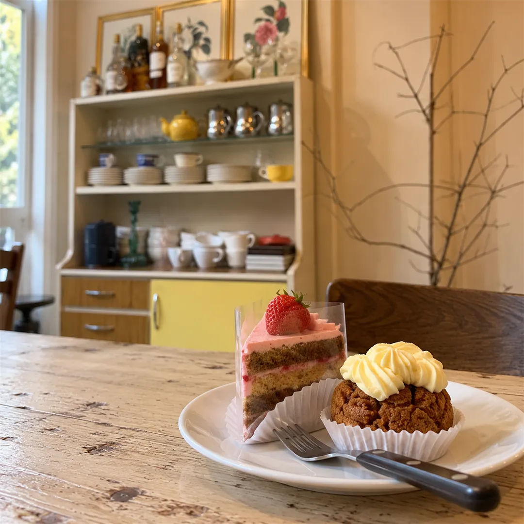 Pink strawberry cake slice and a cream-topped pastry on a white plate on a worn wooden table