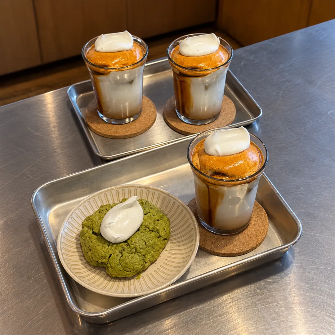 Metal counter with trays of cream coffee and a green scone
