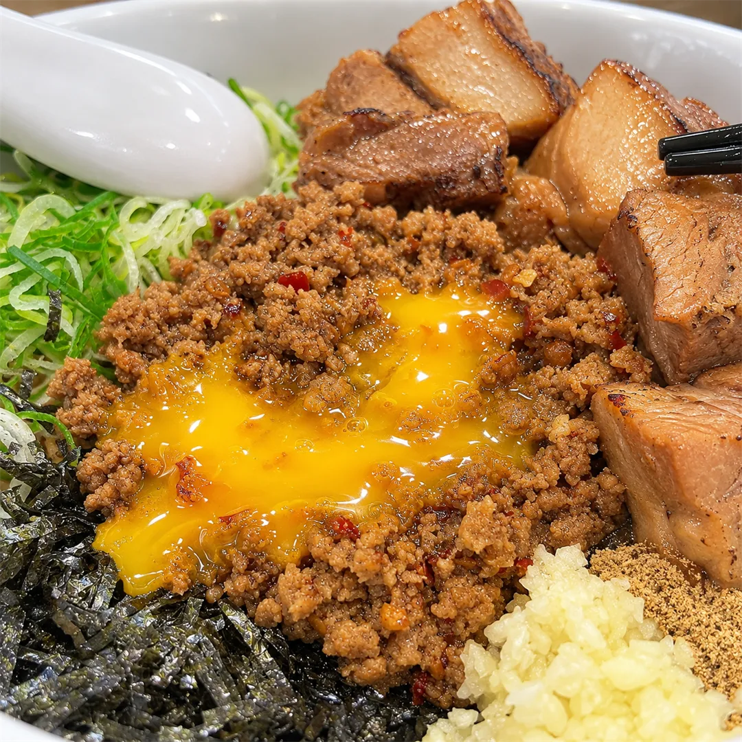 ภาพใกล้ของไข่แดงที่แตกบนเนื้อสับ มีสาหร่าย หมูชาชู ช้อนและตะเกียบ