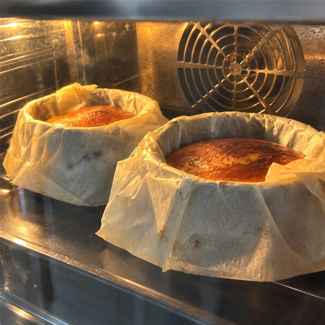 Two round molds lined with baking paper holding baked cakes inside an oven
