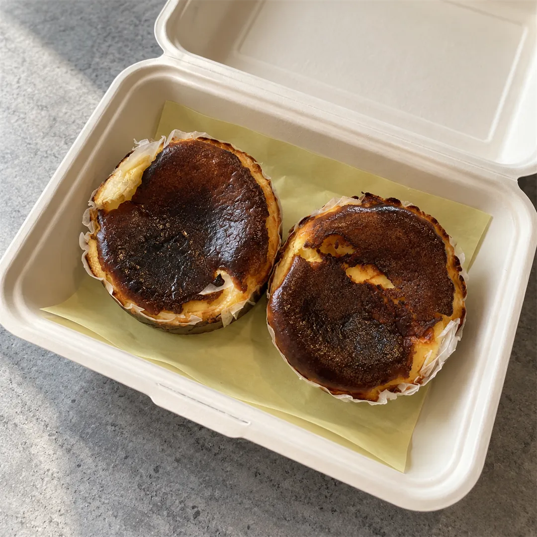 Takeaway box holding two Basque cheesecakes in paper cups