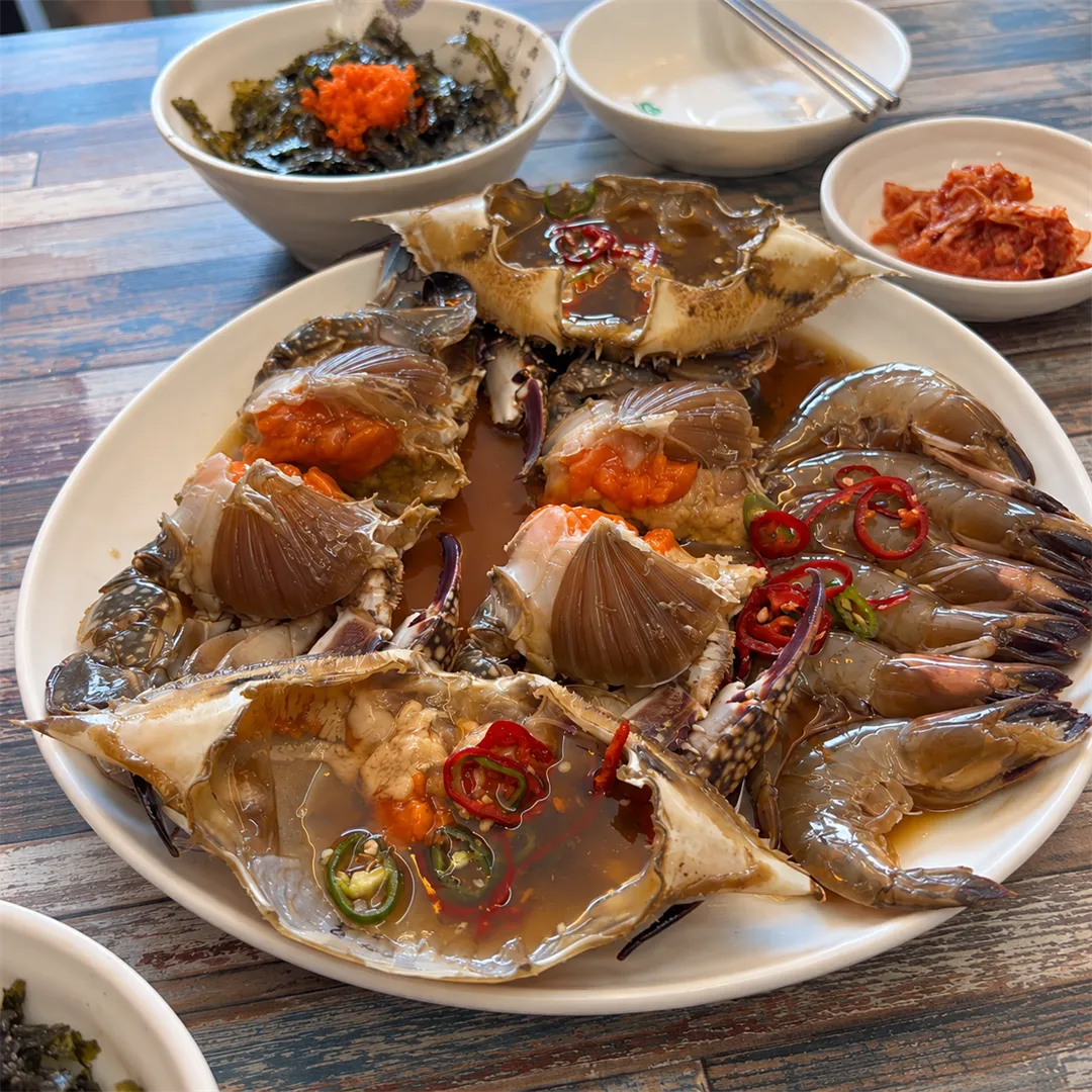 ปูดองซีอิ๊วบนจานรีสีขาว มีไข่ปูสีส้มและพริกแดงเขียว ด้านหลังมีข้าวใส่สาหร่ายกับไข่ปลา