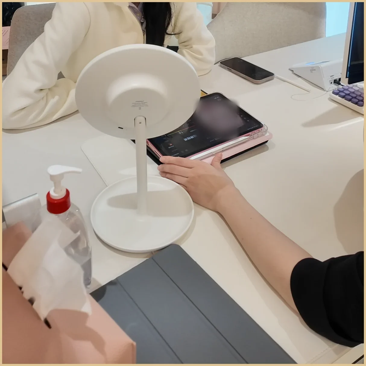 Consultation desk with a round mirror, a tablet showing a skin-analysis screen and a pump bottle; no treatment product is shown