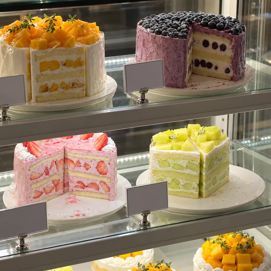 Glass showcase with whole fruit cakes and cut cakes on separate shelves