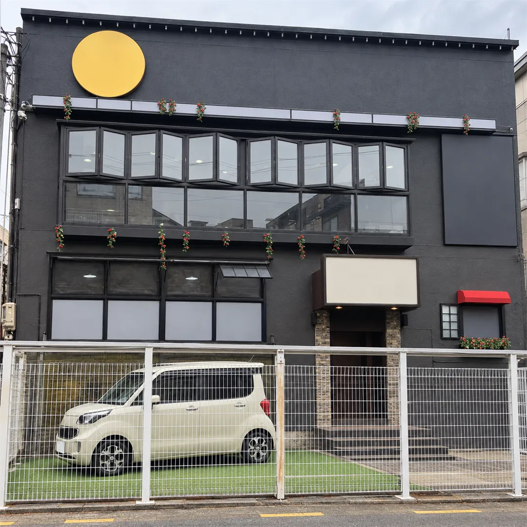 Black two-story building with a red awning and a white mesh fence in front