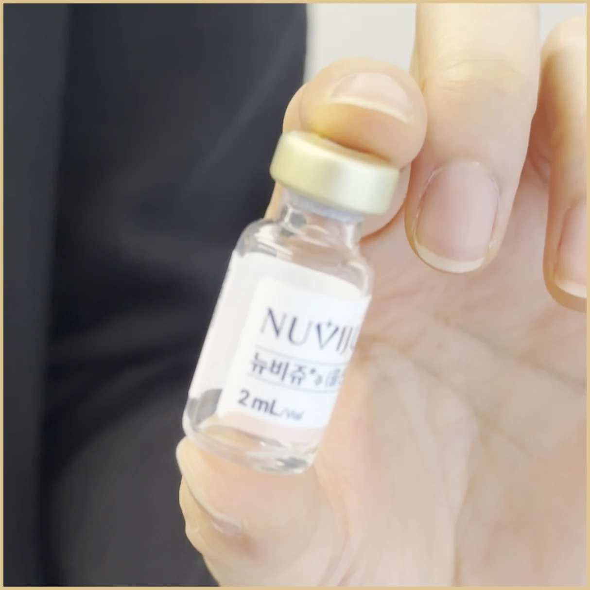 A hand holding a small glass vial with a gold-colored cap and a label showing NUVIJU lettering and 2 mL