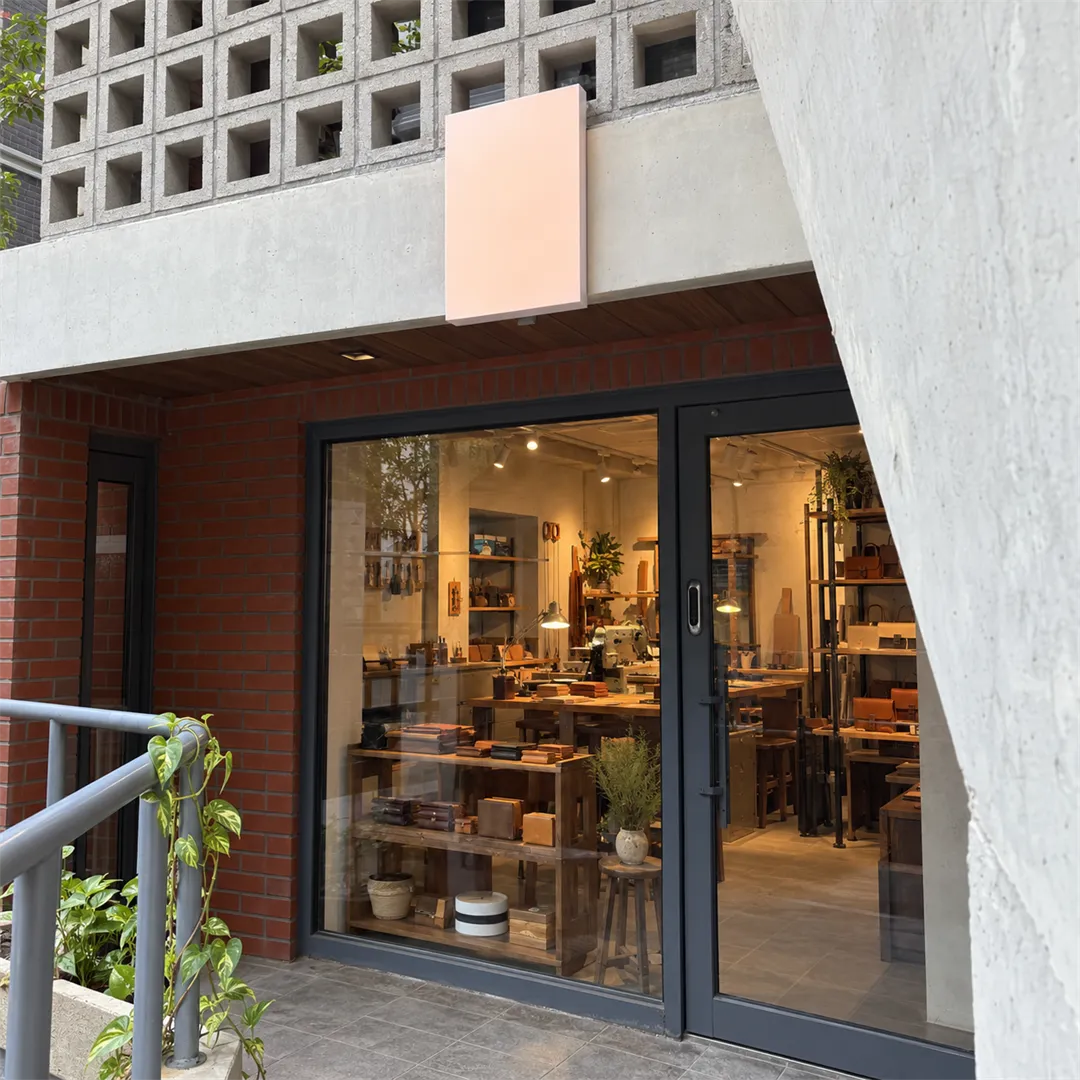 Concrete block wall above a blank light pink sign panel, red brick, a grey railing and a lit glass storefront with shelves and a sewing machine inside