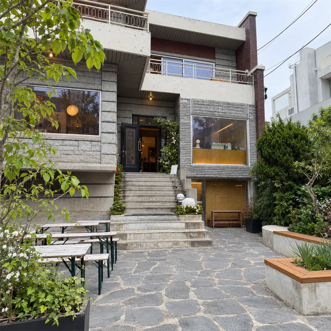 Grey house-style cafe with a central staircase, benches and a stone courtyard with outdoor tables