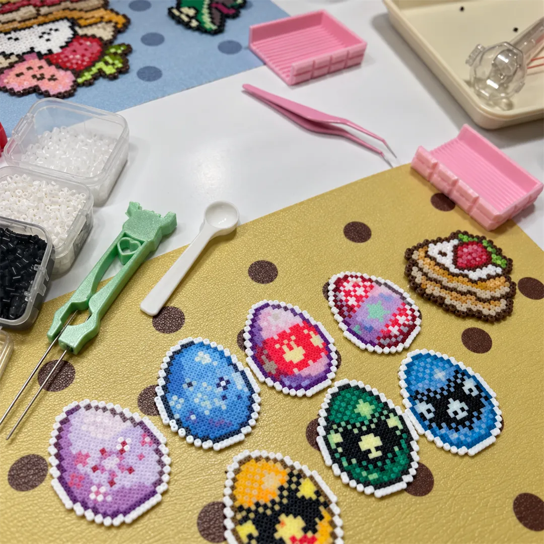Oval pixel bead pieces in purple, blue, red and green on a mustard mat with tweezers and bead scoops