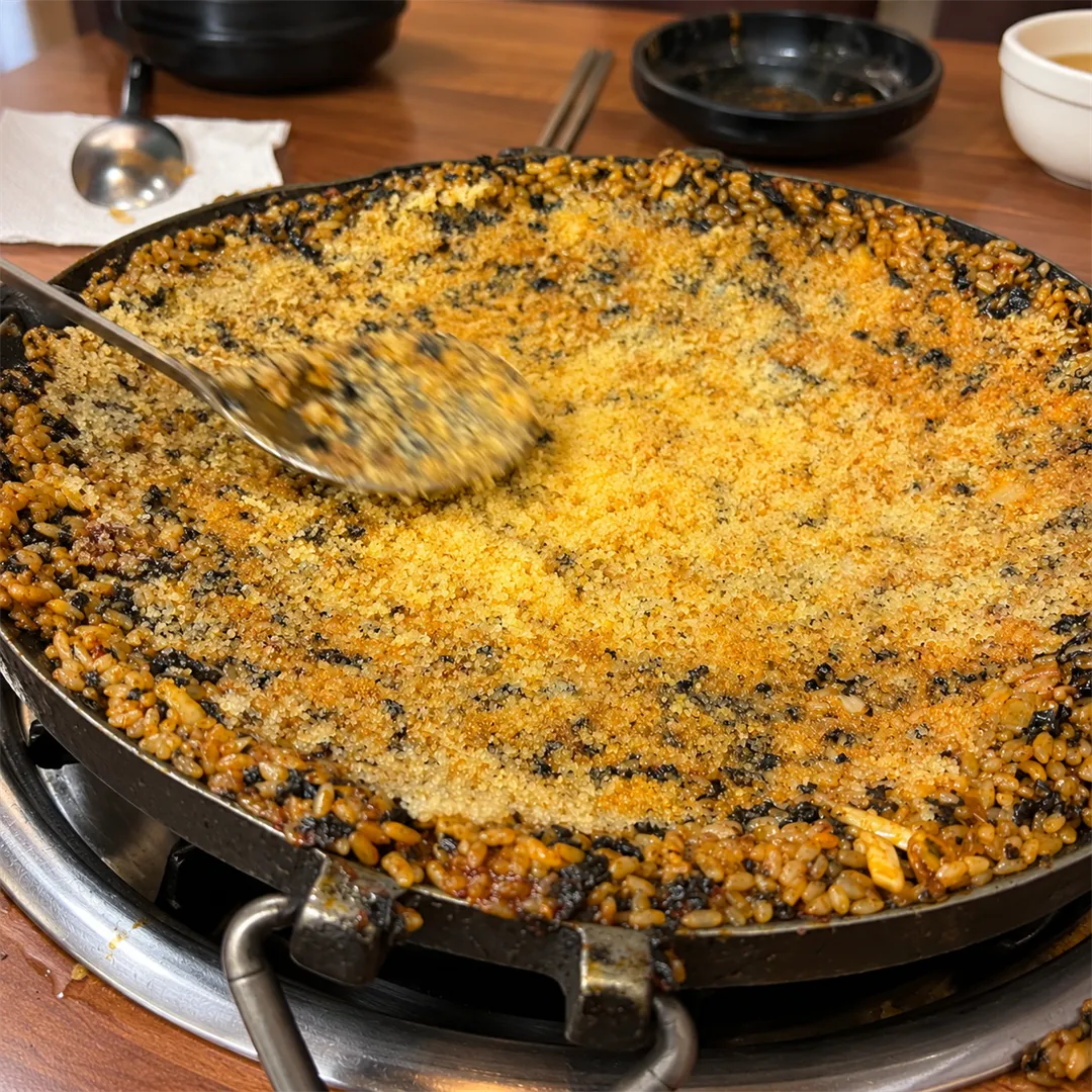 ข้าวผัดบนกระทะกว้าง มีช้อนปาดไข่ปลาสีเหลืองและสาหร่ายที่ขอบ