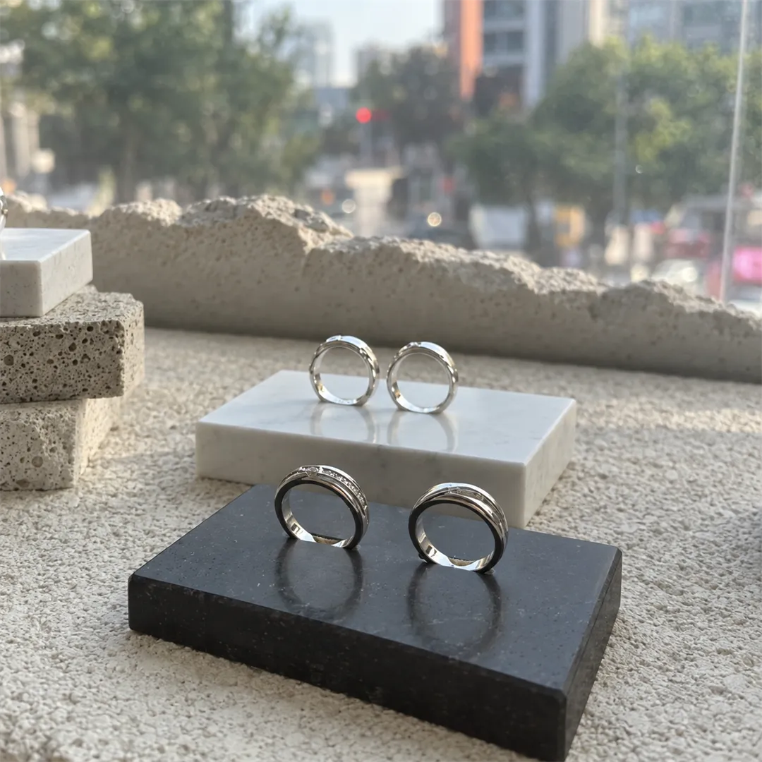 Silver couple rings on white and black stands on a stone display shelf by the window