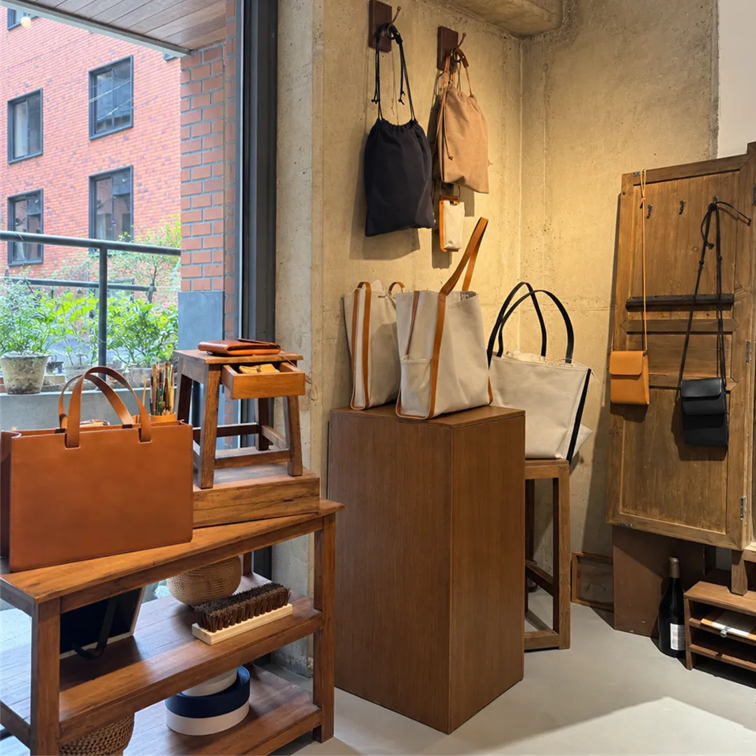 Pouches hung on a concrete wall corner and canvas tote bags on a wooden step, with a red brick building seen through the window