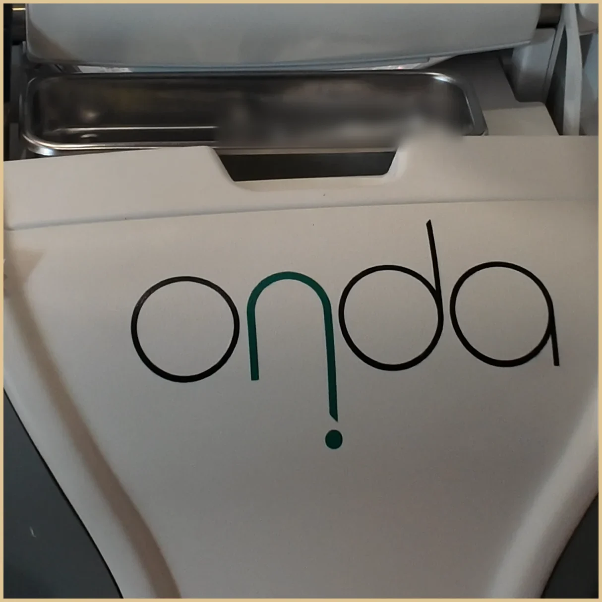 Front of a cart-mounted treatment device with the ONDA name printed in large letters; the screen and settings are outside the frame and the tray contents are blurred.