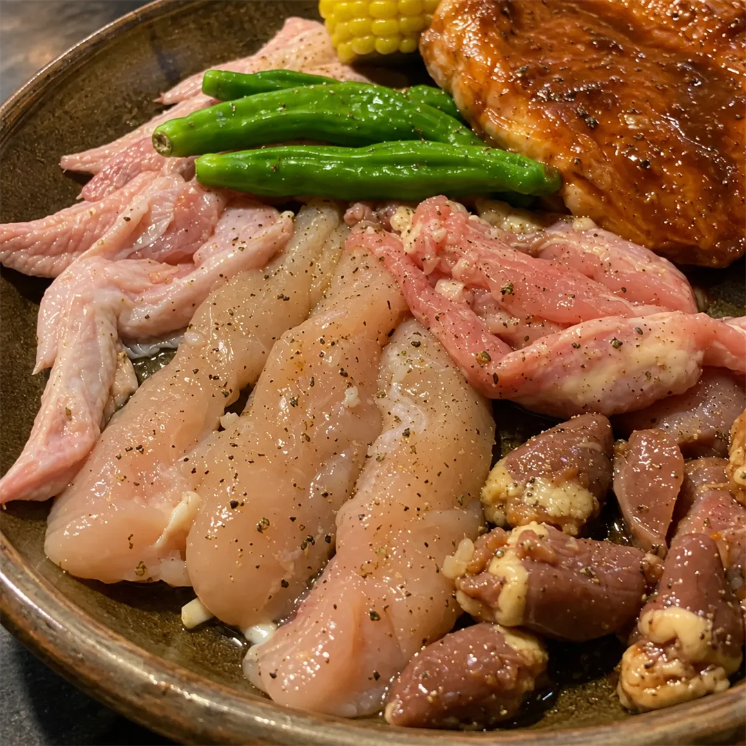 จานกลมสีน้ำตาลมีชิ้นไก่ดิบหลายส่วน พริกเขียว ข้าวโพด และชิ้นไก่หมักซอสแดง