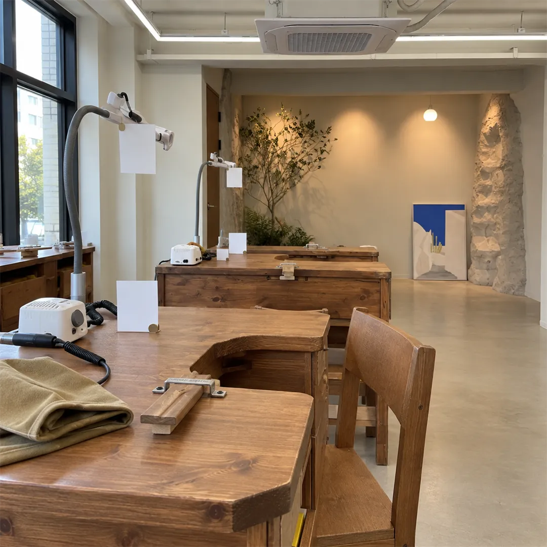 Warm wooden work benches in a ring workshop with window light, plants and a stone pillar