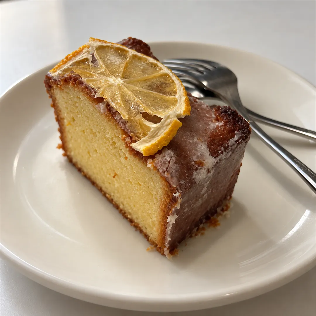 Pound cake slice topped with a dried lemon slice on a round white plate with two forks