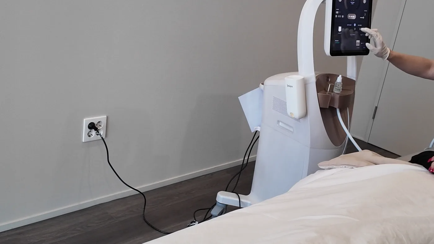 Treatment room console with its touchscreen raised on a white arm and a gloved hand reaching toward the screen