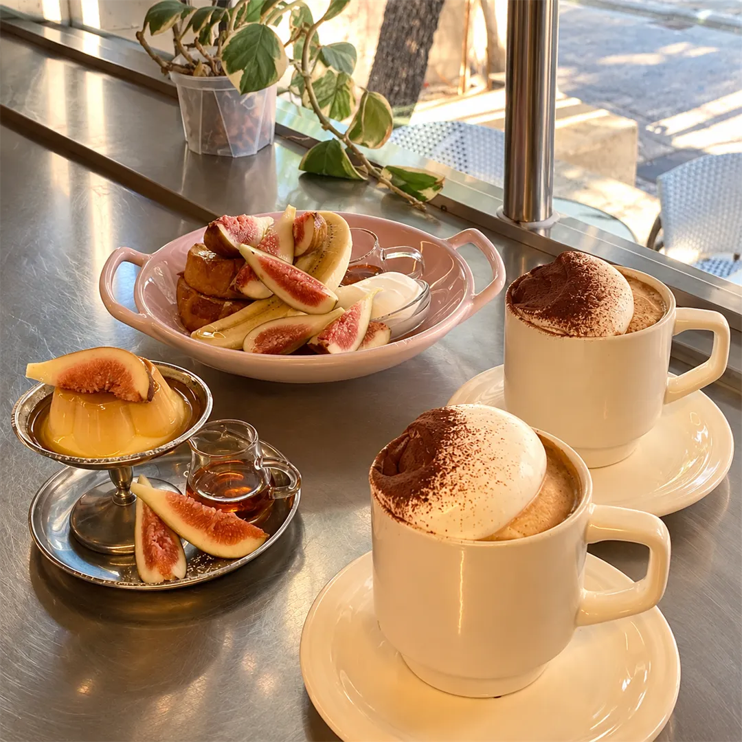โต๊ะสแตนเลสริมหน้าต่างมีเฟรนช์โทสต์ท็อปมะเดื่อและกาแฟที่มีครีมด้านบน แสงสว่างจากหน้าต่าง