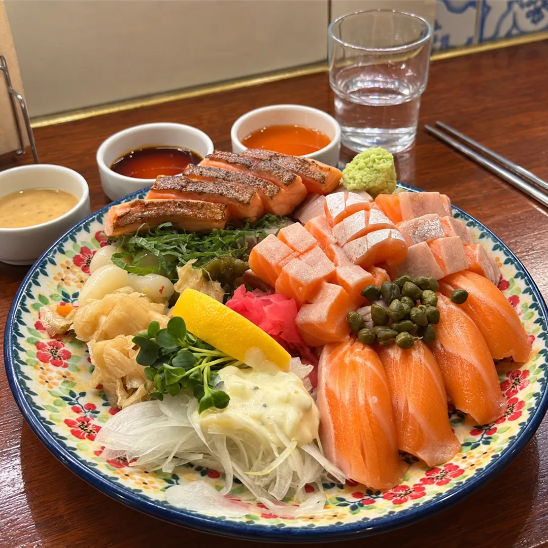 Raw salmon, seared salmon, capers and lemon on a floral plate with sauce dishes