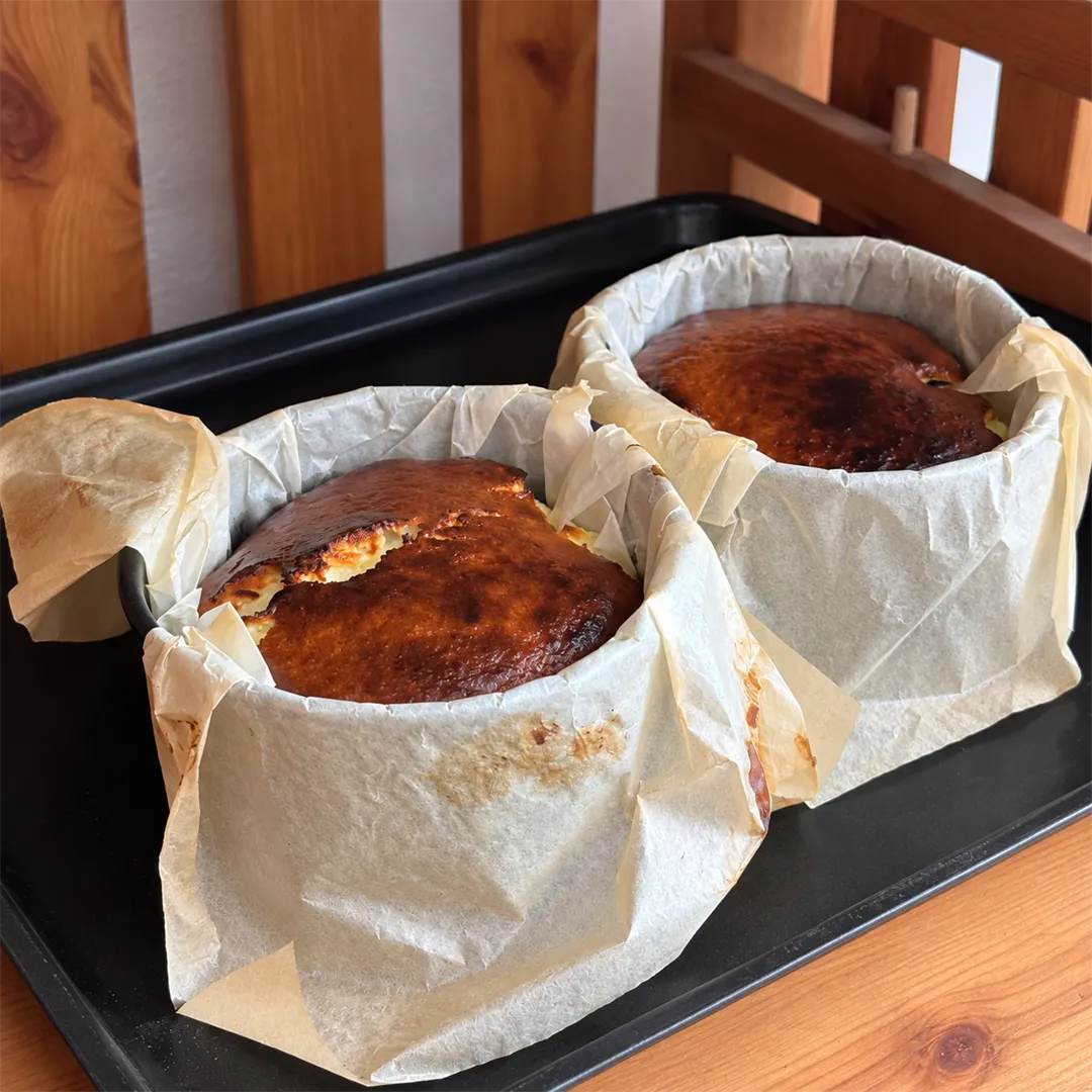 Two baked Basque cheesecakes in baking paper molds on a black tray
