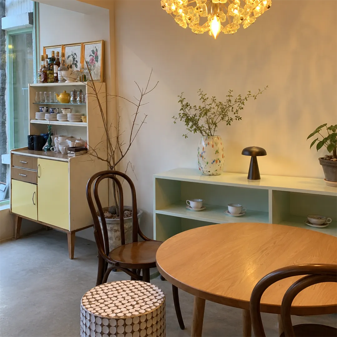 Pale cabinet with yellow doors, a low mint shelf with cups and plates, a mushroom lamp and a glass chandelier