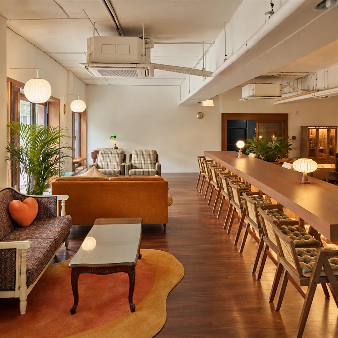 Cafe hall with long wooden tables, rattan chairs and patterned sofas with orange heart cushions