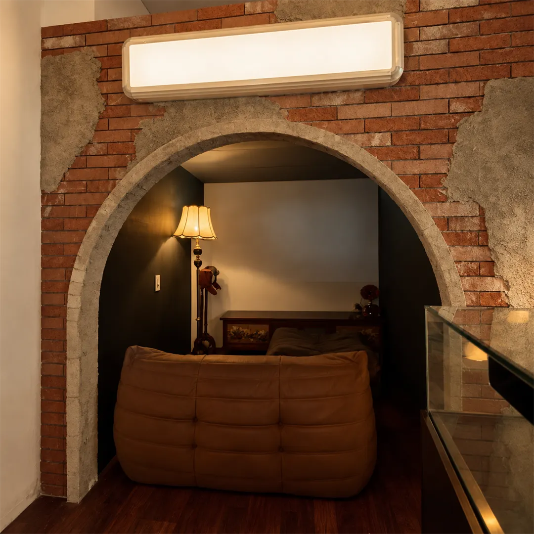 Brick and cement arch with a curved brown sofa, a lamp and a grey projection wall