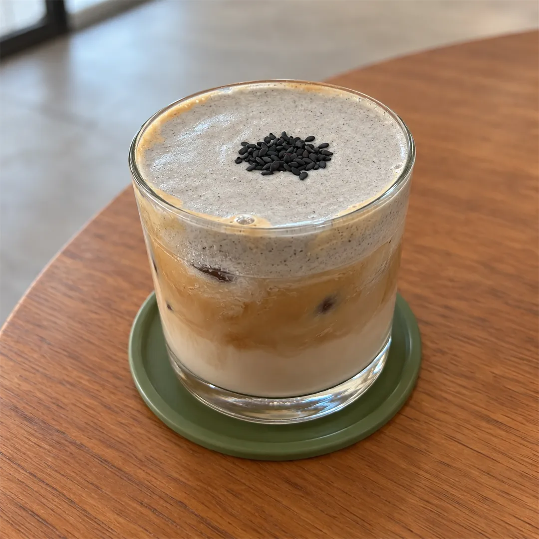 Drink with grey foam topped with black sesame on a tray at the pond edge