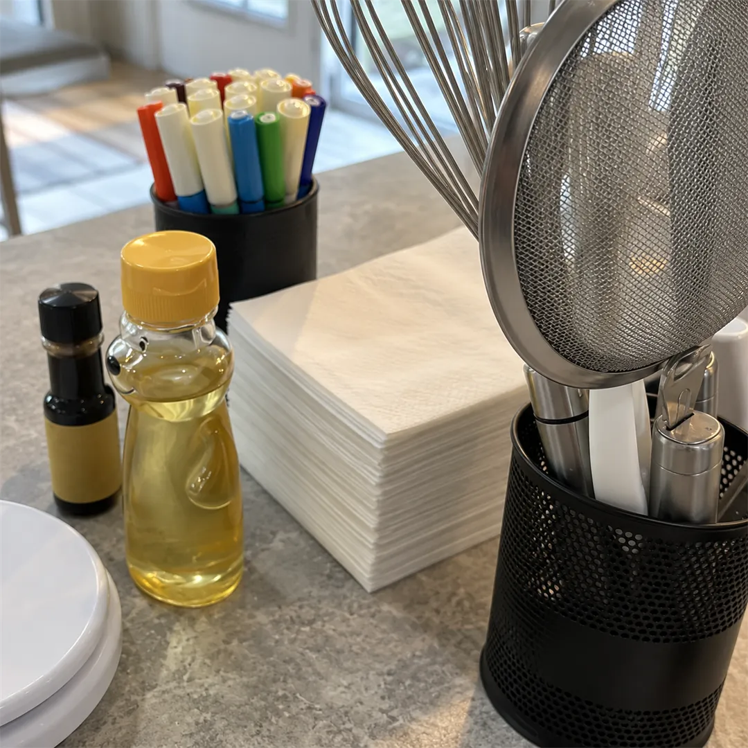 Black perforated holder with balloon whisks, a fine sieve and spatulas, beside a marker holder and a bear-shaped bottle