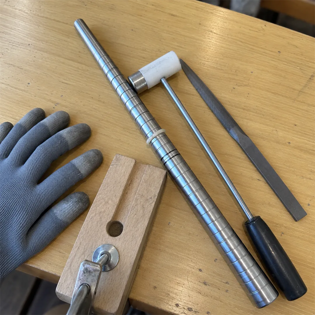 Wooden work bench with a ring mandrel, a hammer, a file and a gloved hand
