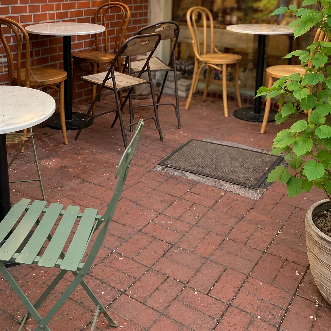Red brick terrace with a white round table, bentwood chairs, a mint folding chair and a large-leaf plant