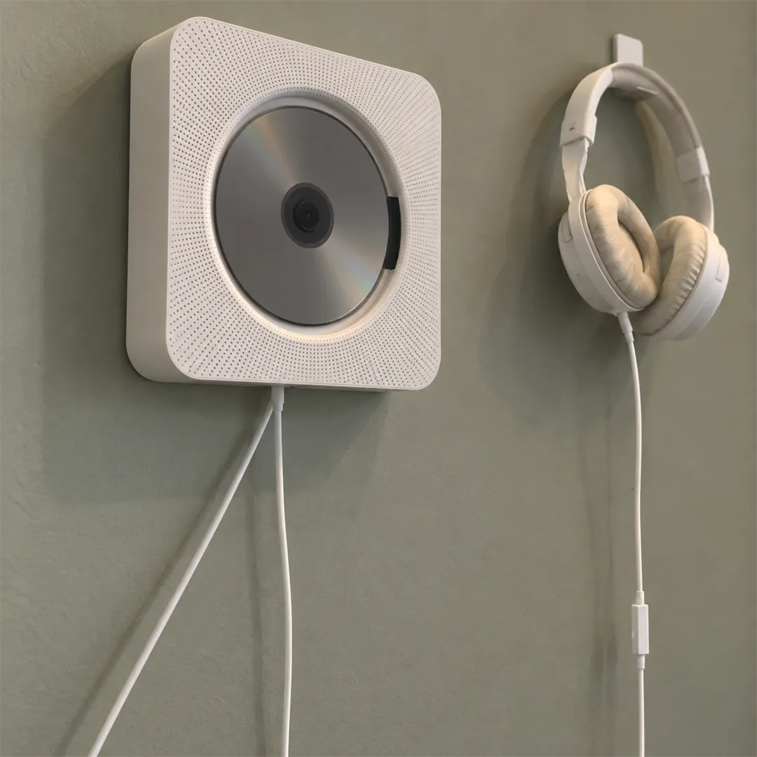 White wall-mounted CD player with a silver disc and white headphones hanging on a grey-green wall