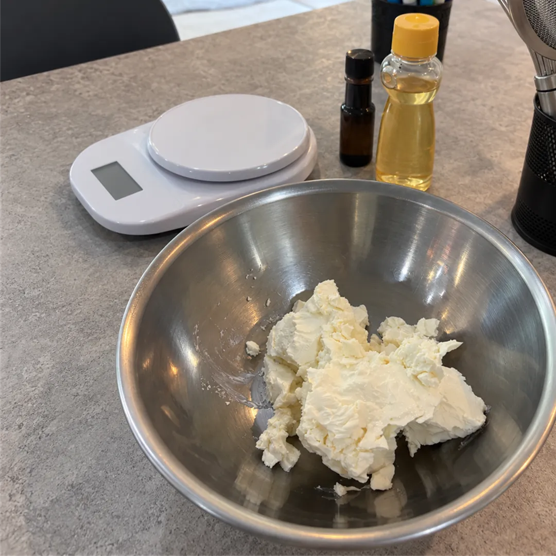 Steel bowl of cream cheese and a white scale with an oil bottle on a grey stone counter