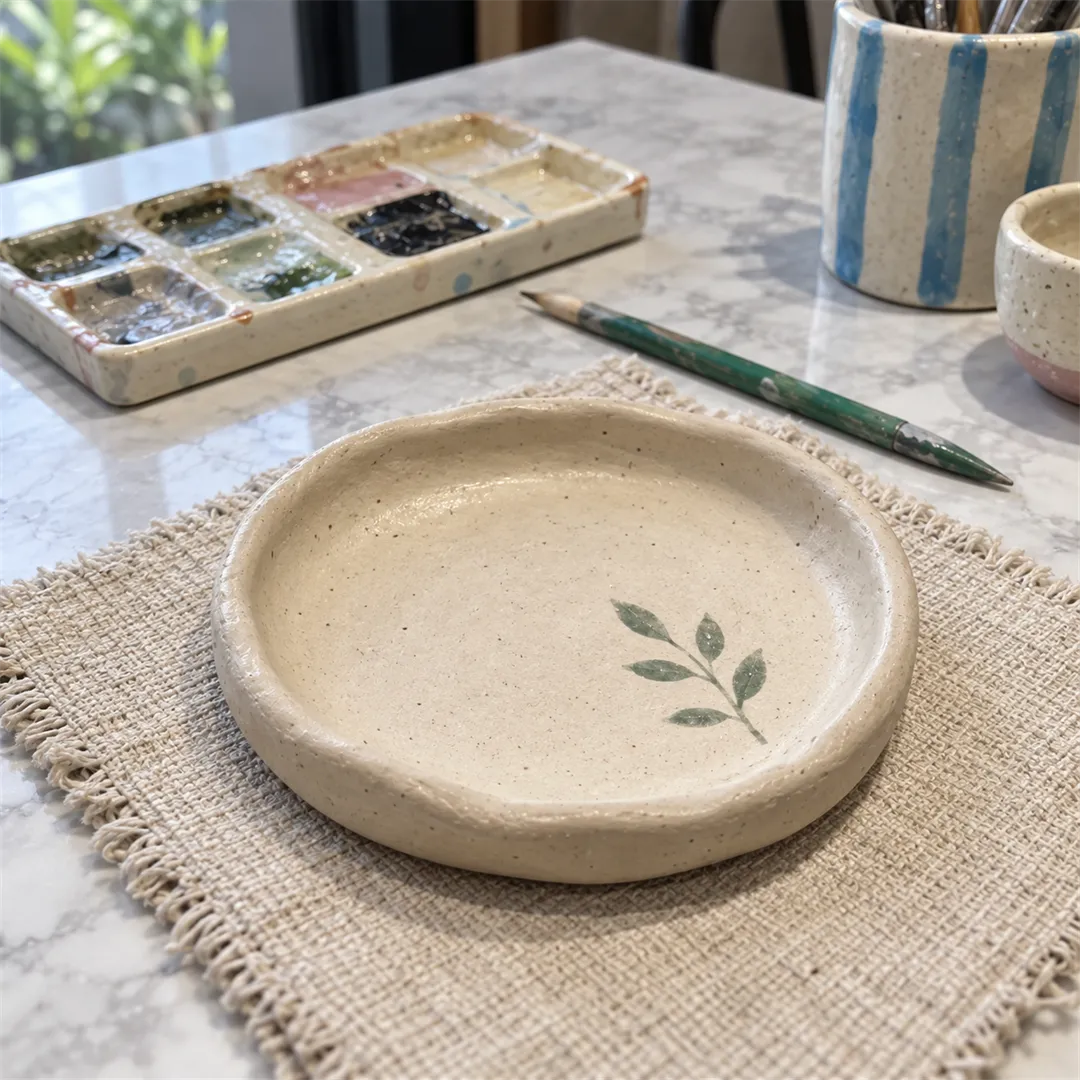 Round plate with green leaf patterns beside a palette and a green stick on a work table