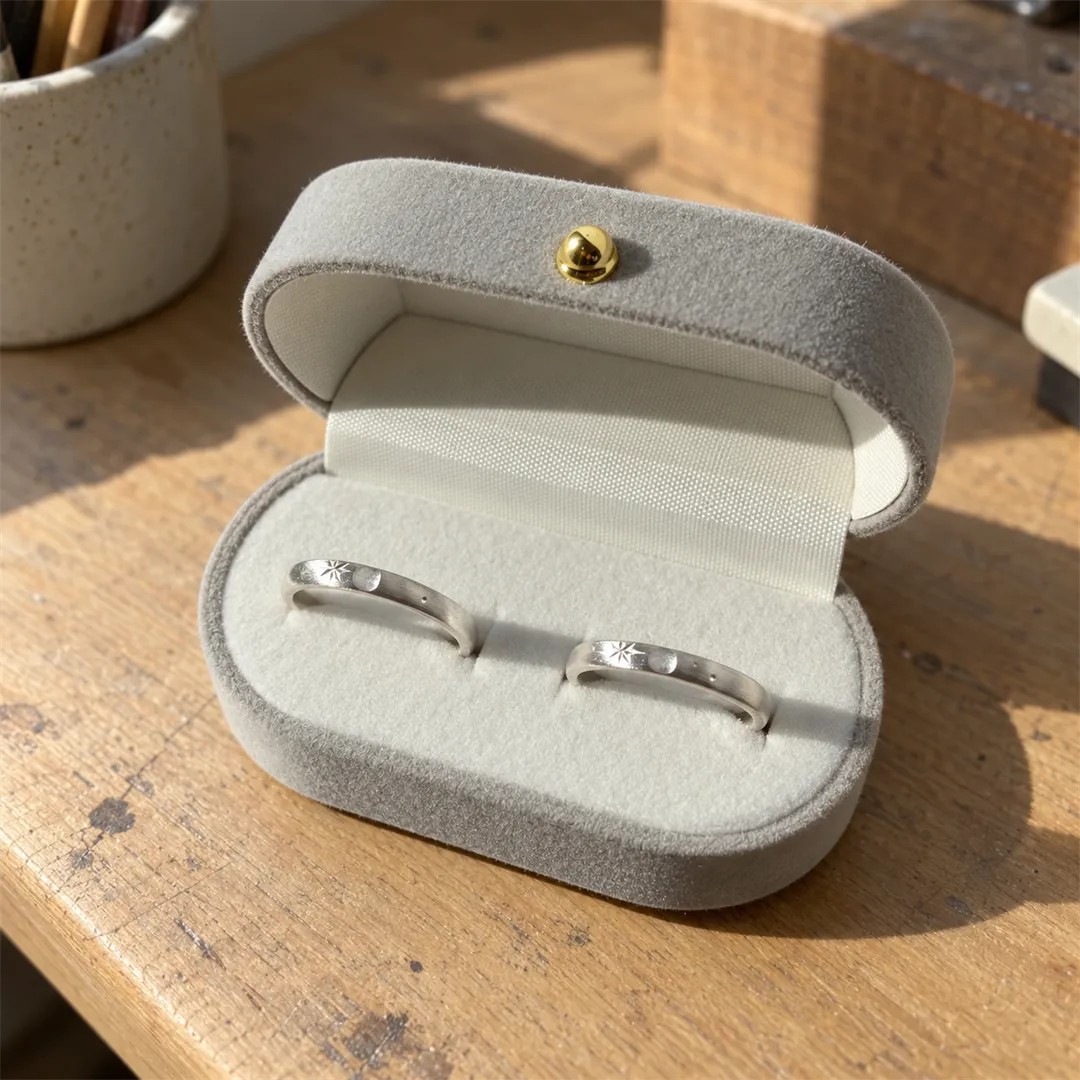 Silver star-pattern ring in a ring case beside a gold button