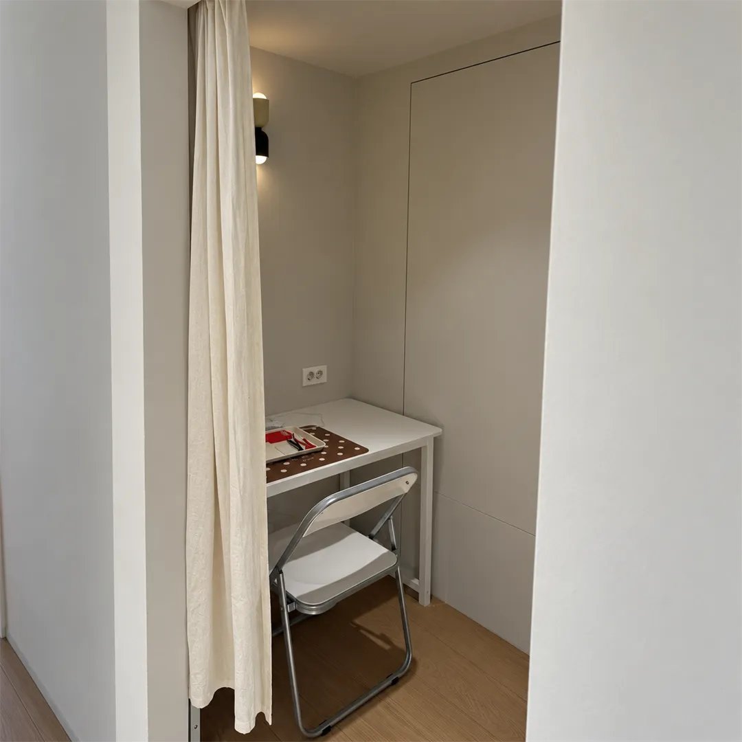 Small curtained booth with a white table, a brown polka-dot mat, a red tray and tweezers
