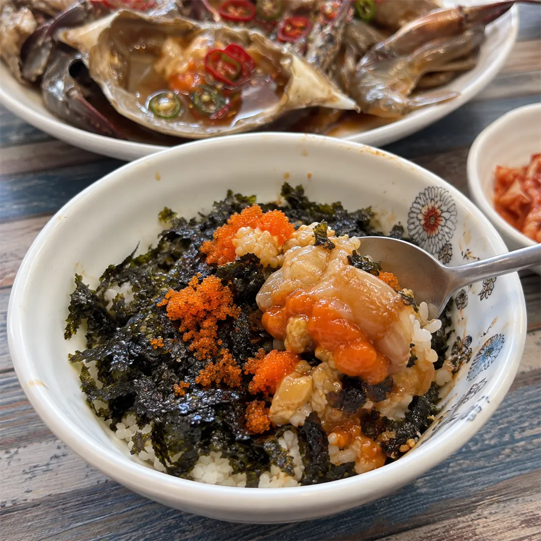 ข้าวใส่สาหร่ายและไข่ปลาสีส้มในชามลายดอกไม้ มีช้อนตักเนื้อปู ด้านหลังเป็นปูดองซีอิ๊ว