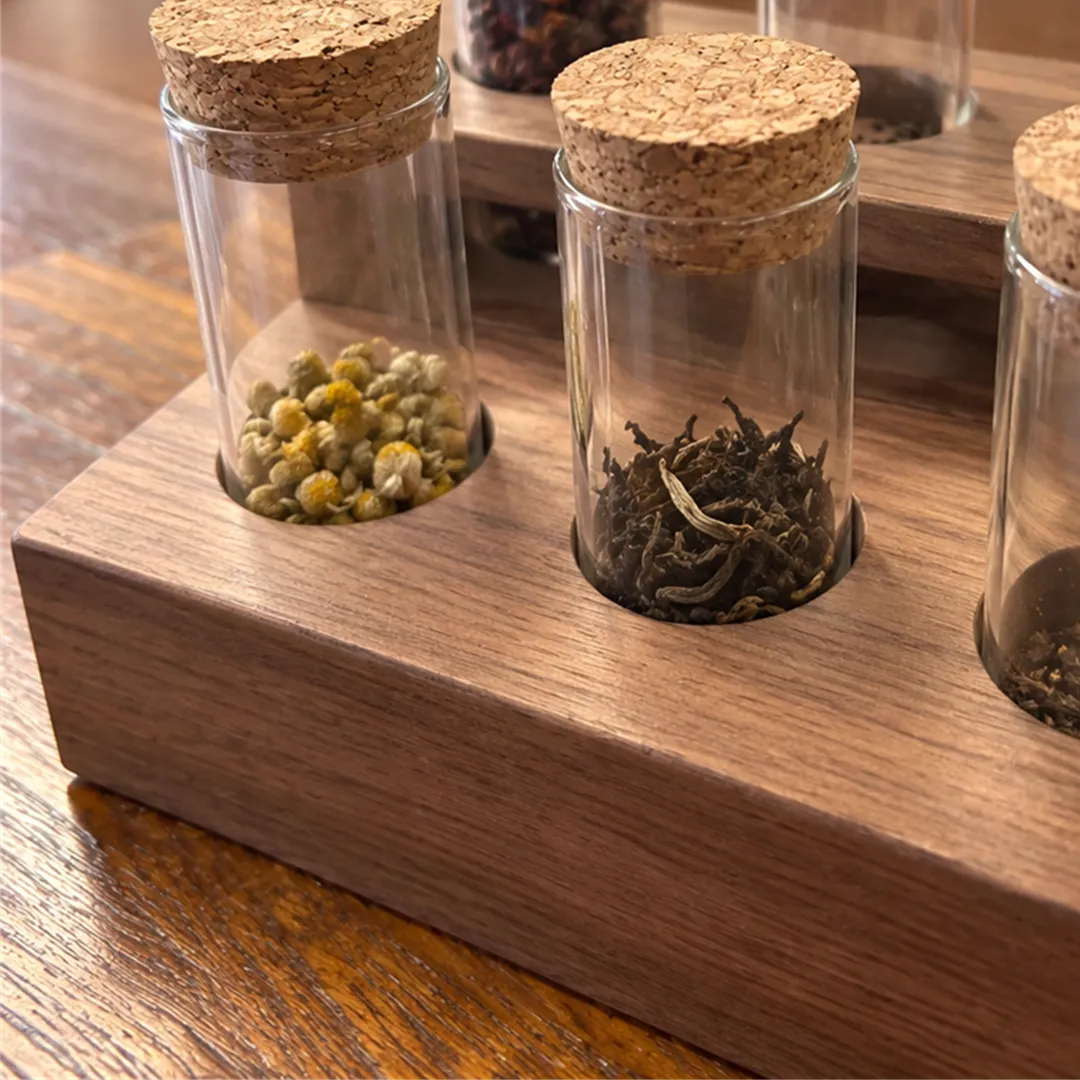 Cork-stoppered glass jars with dried yellow flower buds, dark tea leaves and red dried fruit on a wooden stand