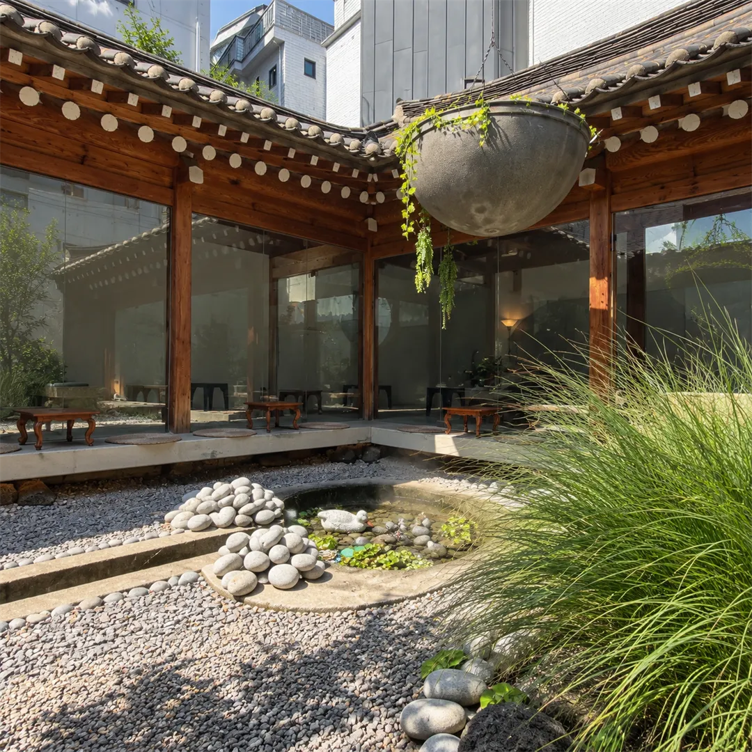 Hanok cafe courtyard with tiled eaves, wooden pillars, a pond with stones and pampas grass