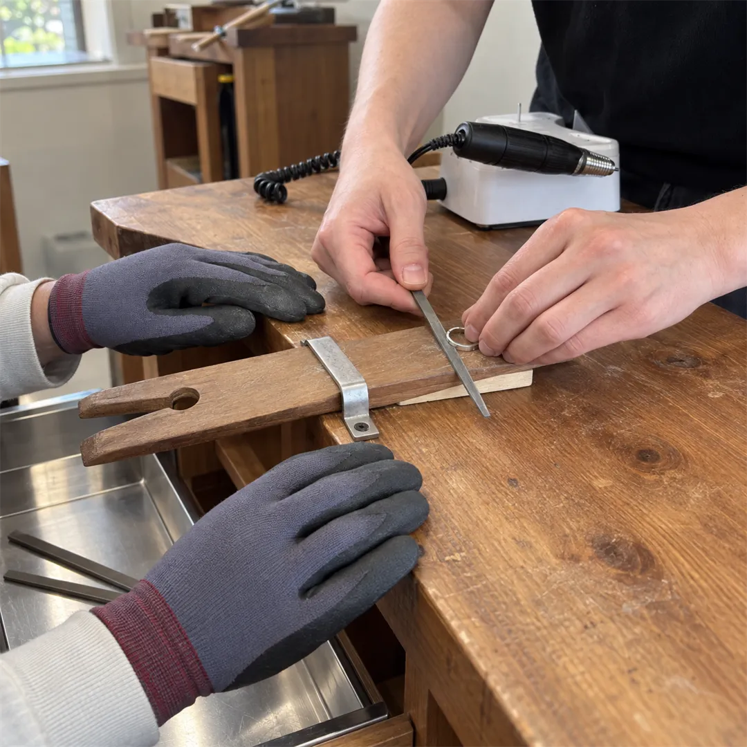 Gloved hands filing a ring on a wooden bench with a bench pin, a handpiece and a control box