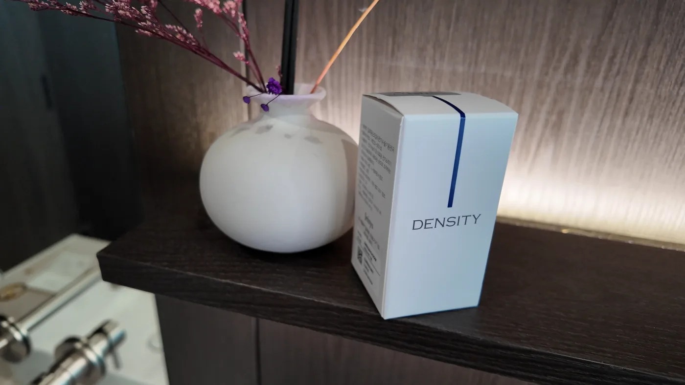 กล่องสีขาวพิมพ์คำว่า DENSITY วางข้างแจกันสีขาวบนชั้นในห้องทำหัตถการ